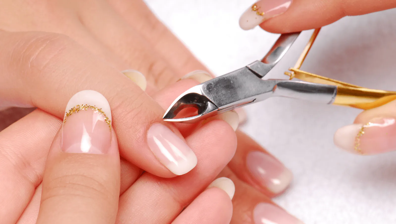 Cuticle nipper trimming around short nude nails with a thin gold accent line