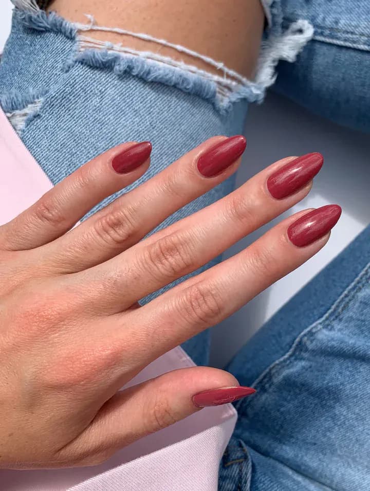 Medium almond nails in glossy brick red, hand resting on denim