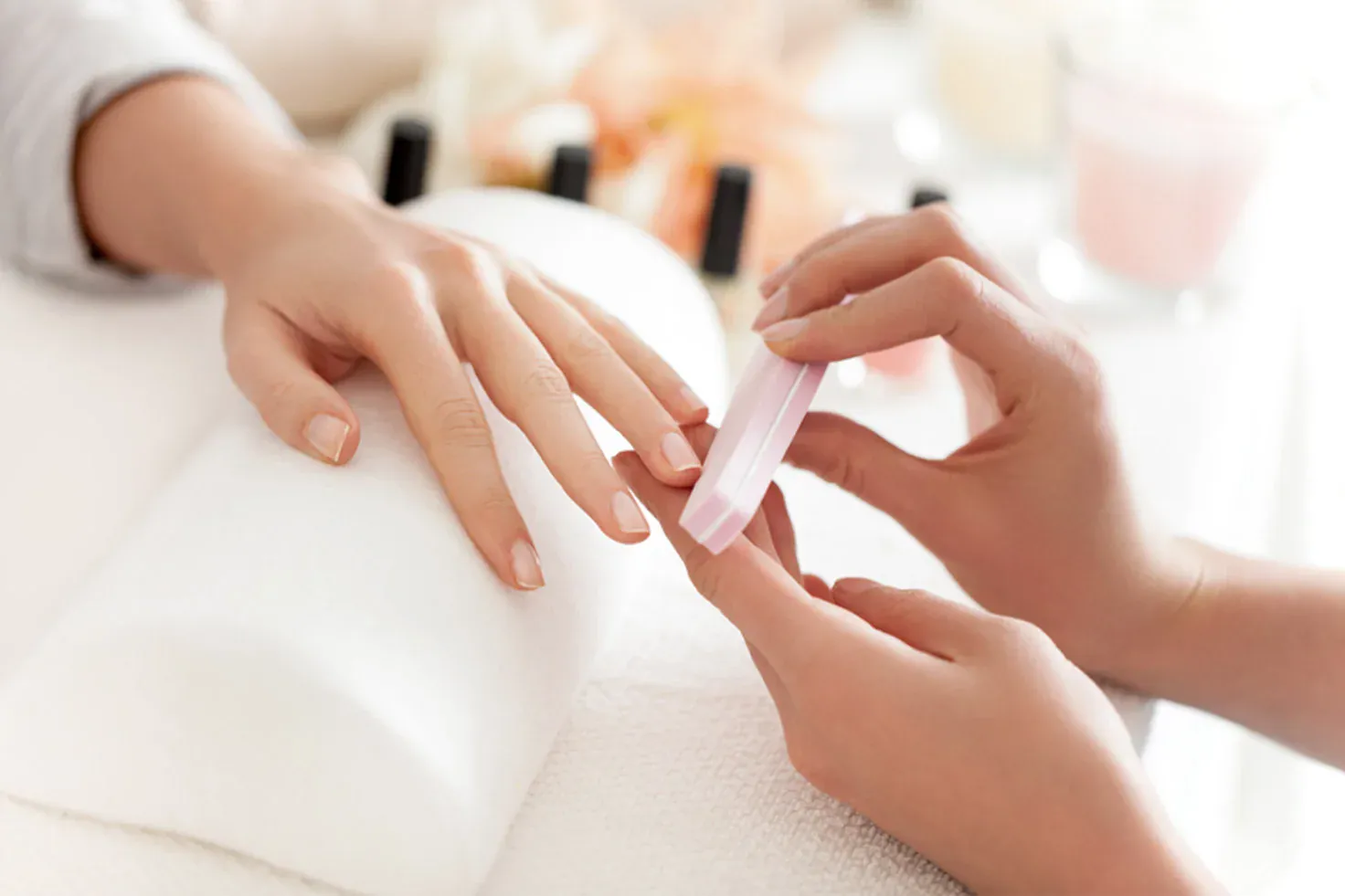 Nail technician filing natural nails on a manicure cushion