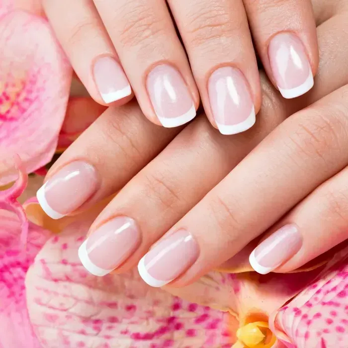 Short square natural nails with a classic white French tip in front of a pink orchid