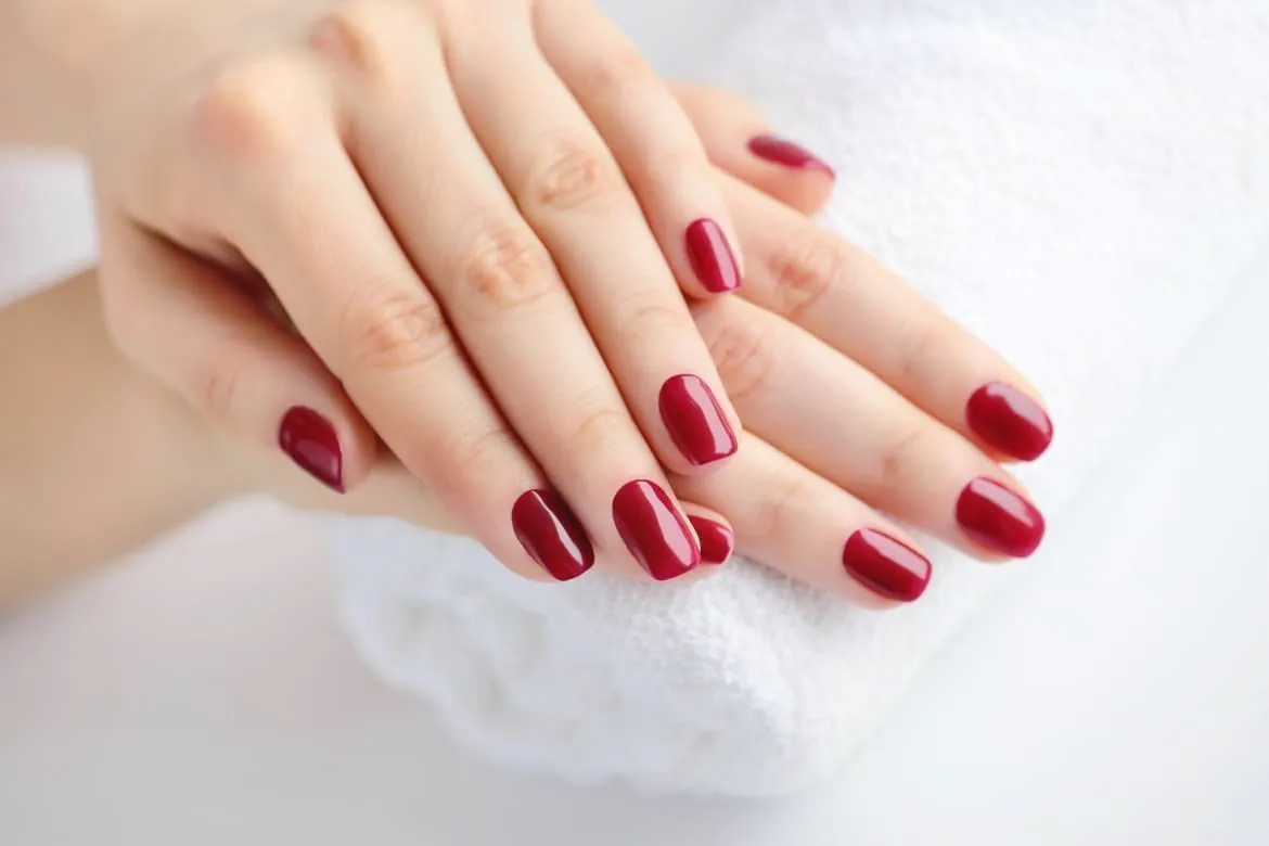 Short oval nails in glossy deep red, hands resting on a white towel