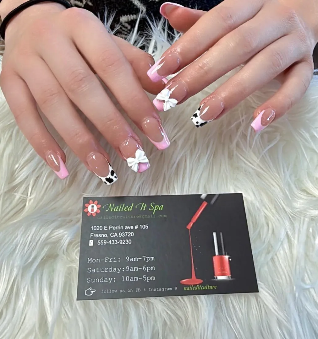 Long square nails with pink French tips, white 3D bows and cow-print accent nails, next to a Nailed It Spa business card